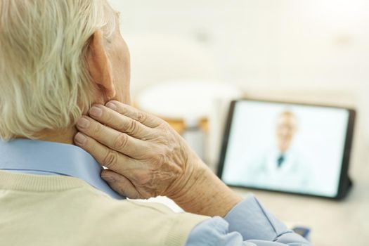 Selective focus photo of grey-haired man touching his neck while video-calling his medical doctor