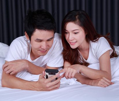 young couple using mobile phone on bed in the bedroom