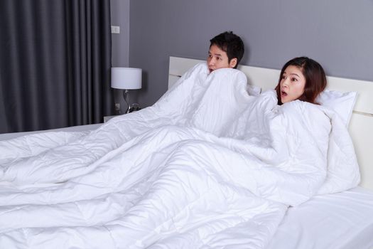 young couple watching scared movie under the blanket on bed