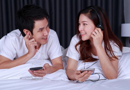young couple listening music from mobile with headphone on bed