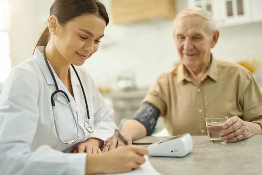 Smiley female doctor making notes while examining senior man sitting beside her