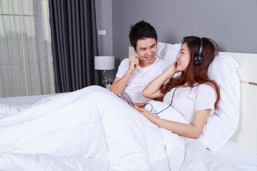 young couple listening music from mobile with headphone on bed