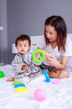 baby playing toys with mother on bed at home