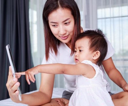 Mother and baby are looking to play and read tablet computer on bed at home