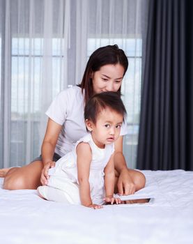 Mother and baby are looking to play and read tablet computer on bed at home