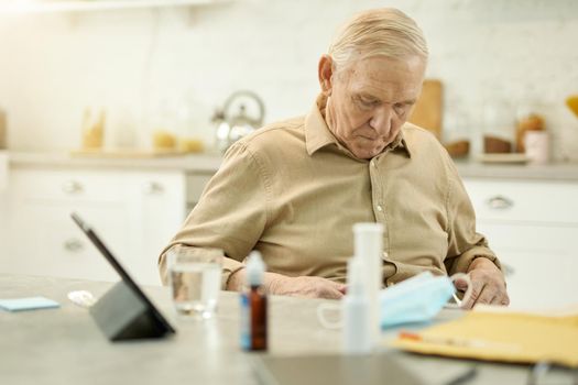 Serious senior man sitting at the table and holding his hands on his stomach