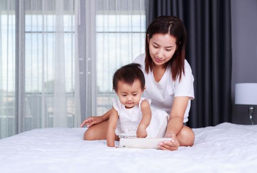 Mother and baby are looking to play and read tablet computer on bed at home
