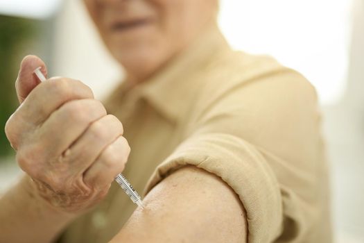 Cropped photo of elderly gentleman holding syringe and sticking it in his arm while injecting medicine