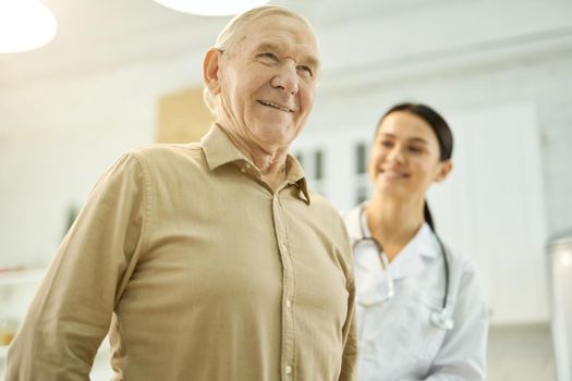 Joyous senior gentleman standing tall while medical worker checking his posture