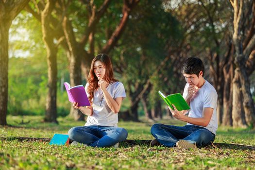 man and woman sitting and reading a book in the park