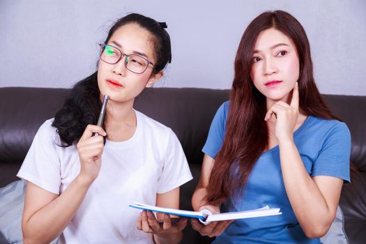 two young woman thinking with a book on sofa in living room at home