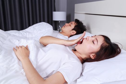 young woman yawning and her husband sleeping on bed