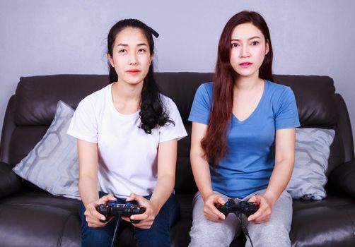 two young woman using joystick controller playing video game on sofa in living room at home