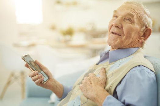 Senior citizen holding mobile phone and talking online with a doctor while holding a heart with his hand