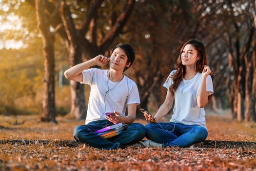 young couple listening music from mobile with headphone in the park