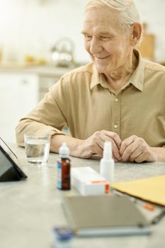 Joyous senior man smiling while sitting at table full of medical supplies and notes