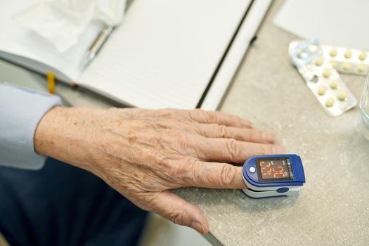 Cropped photo of hand of eldelry man with a fingertip pulse oximeter clipped on finger