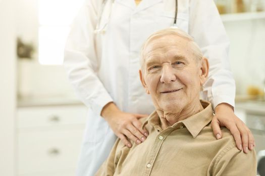 Cropped photo of a happy senior citizen sitting down and doctor in white uniform standing behind him