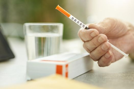 Cropped photo of hand with a thin medical syringe near a glass of water and box of medication