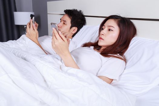 young couple using mobile phone on bed in the bedroom