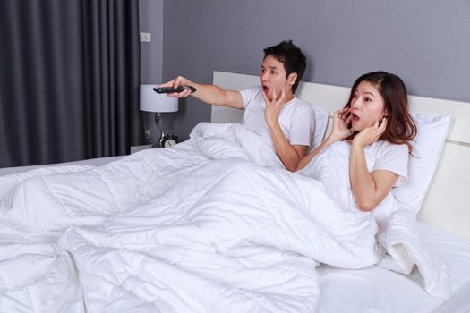 young couple watching scared movie with tv remote control on bed