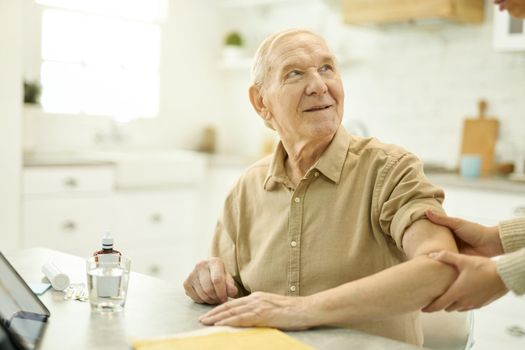 Senior citizen looking hoopeful while having his shoulder examined by medical worker at home