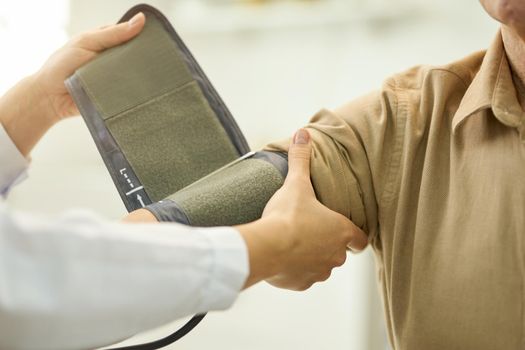 Fragment photo of medical worker in white lab coat securing inflatable part of manometer around arm of senior patient