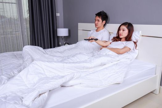 young couple lying on a bed with remote control and watching television in the bedroom