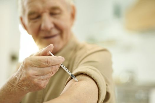 Selective focus photo of a senior man having his sleeve rolled up and giving himself an injection