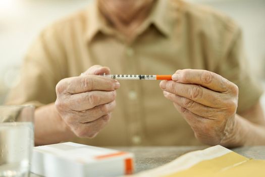 Cropped photo of eldelry person sitting at the table and holding a thin medical syringe