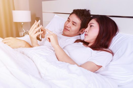 young couple using mobile phone on bed in the bedroom
