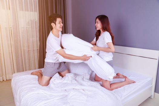 cheerful young couple having a bolster pillow fight on bed in the bedroom