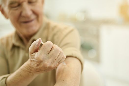 Copy-space photo of a smiley aged man with sleeve rolled up holding syringe and giving himself an injection