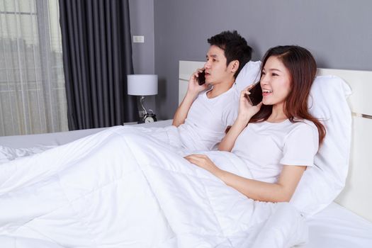 young couple lying in bed and talking on mobile phone
