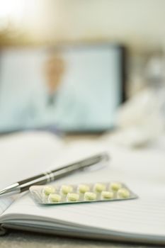 Selective photo of a blister of pills and a pen on top of a notebook laying on the table