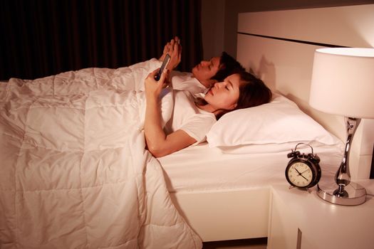 young couple using mobile phone on bed at night