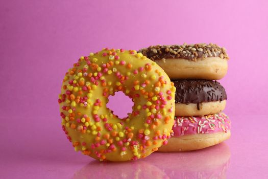 Sweet still life donut berliner close-up at the back lie a stack of three doughnut yellow on a bright pink background copyspace