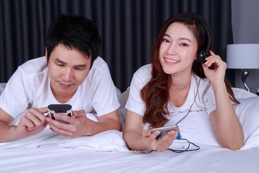 young couple listening music from mobile with headphone on bed