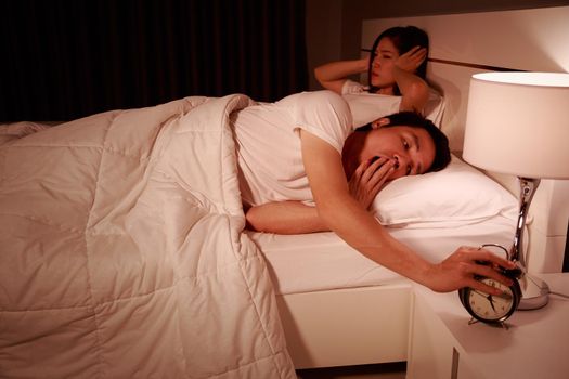 unhappy couple being awakened by an alarm clock in bedroom in the morning
