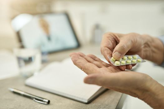 Cropped photo of aged man hands holding blister of pills with tablet screen in the background
