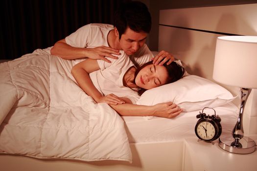sleeping woman lying on bed with a concerned guy comforting her at night