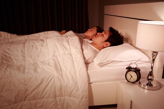 young couple sleeping on a comfortable bed in bedroom at night