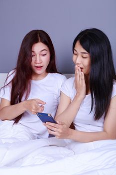 two shocked woman using a phone in her hand on bed in the bedroom