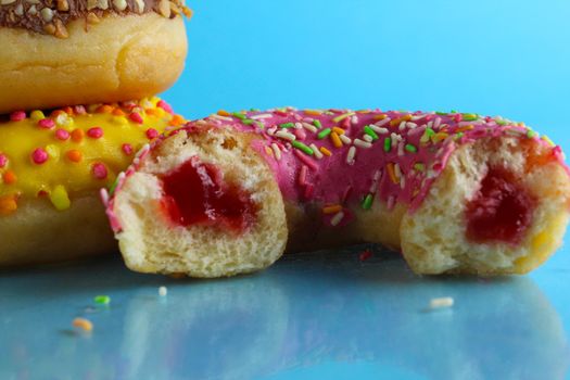 Yellow pink chocolate donuts lie a stack of a row of cut-off bitten doughnut stuffed with pink chocolate on a blue bright background with room for text. still life from