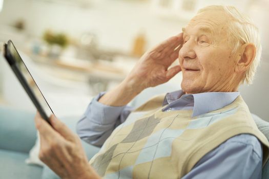 Pensioner holding gadget while looking at the tablet screen and making a video call with doctor
