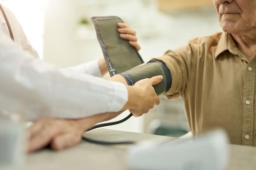 Cropped photo of a certified medic securing inflatable cuff of a manometr around an elderly person arm