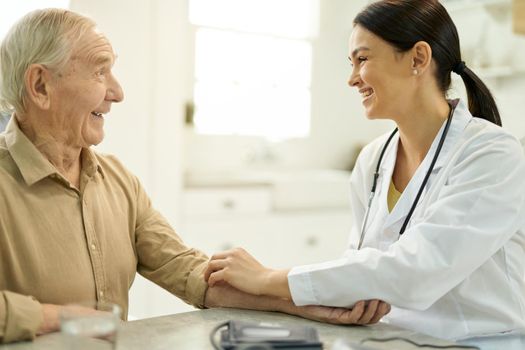 Amicable medic rolling up the sleeve of a cheerful senior man before doing blood pressure check