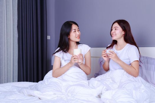 two best friends talking and drinking a cup of coffee on bed in the bedroom 