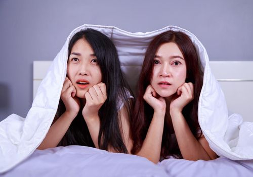 two best friend woman on bed watching a tv with shocked expression on face