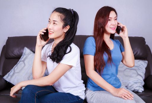 two young woman talking on mobile phone on sofa in living room at home